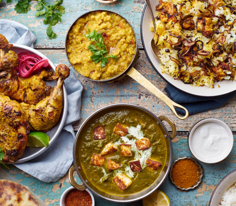 Indian cuisine dinner: tandoori chicken, biryani, red lentil curry dal with rice naan, palak paneer and basmati rice on wooden background